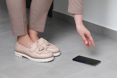 Woman taking dropped smartphone from floor, closeup. Device repairing