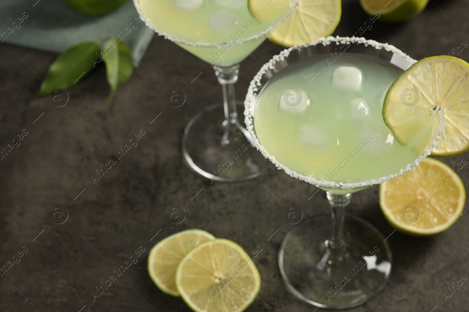 Photo of Delicious Margarita cocktail with ice cubes in glasses and lime on grey table, space for text