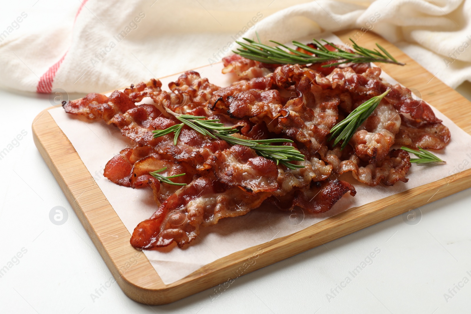 Photo of Slices of tasty fried bacon with rosemary on white table