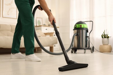 Photo of Professional janitor vacuuming floor in living room, closeup