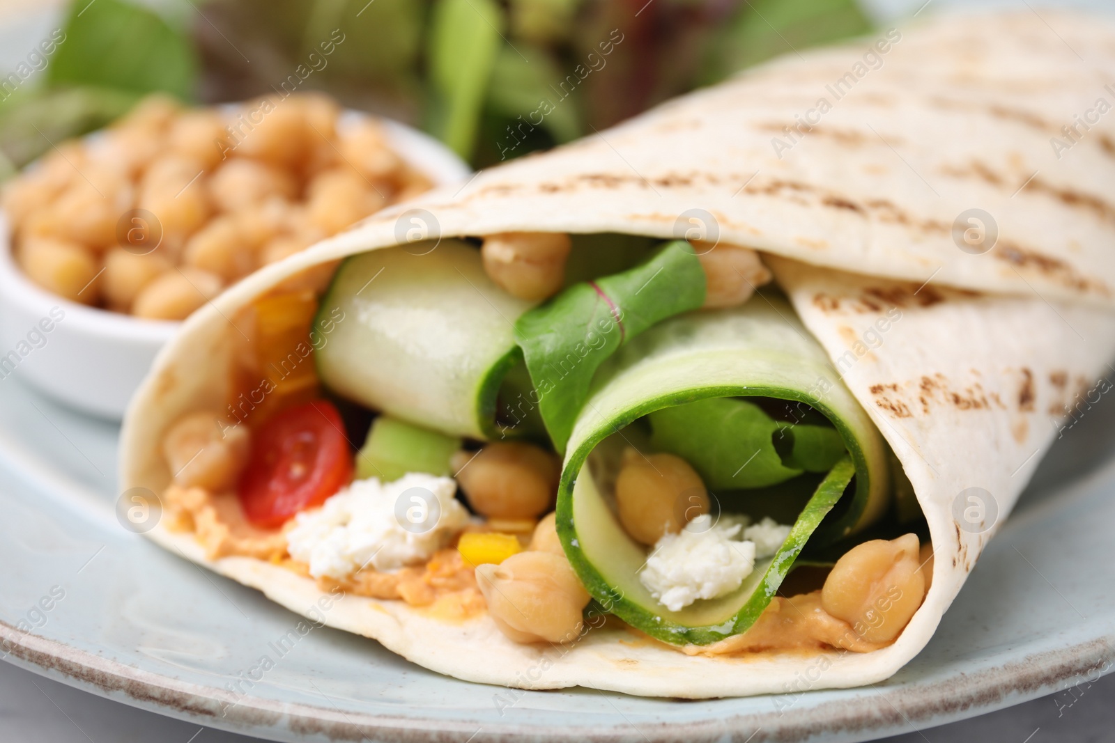 Photo of Delicious hummus wrap with vegetables on table, closeup