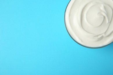 Glass bowl of sour cream on light blue background, top view. Space for text