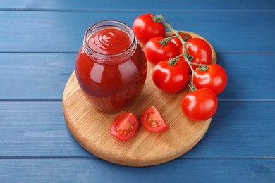 Photo of Organic ketchup in jar and fresh tomatoes on blue wooden table. Tomato sauce
