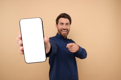 Photo of Handsome man showing smartphone in hand and pointing at it on light brown background, selective focus. Mockup for design