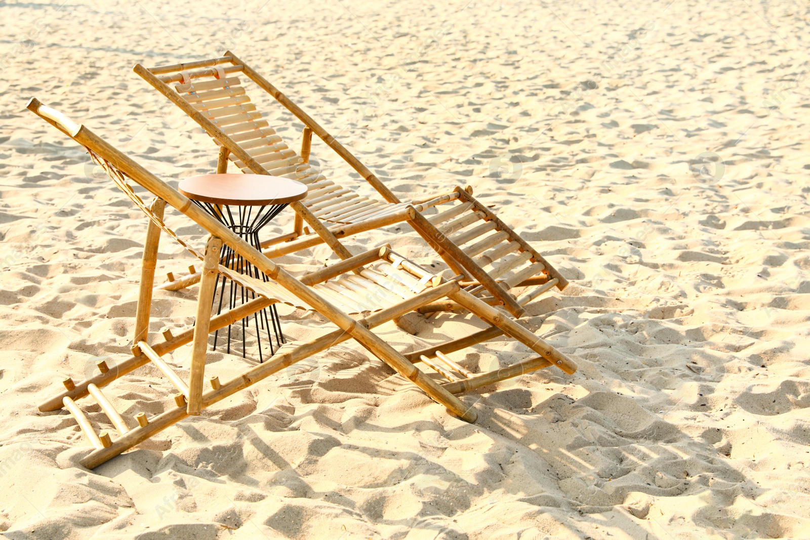 Photo of Empty wooden sunbeds and table on sandy shore. Beach accessories