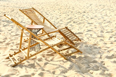 Empty wooden sunbeds and table on sandy shore. Beach accessories