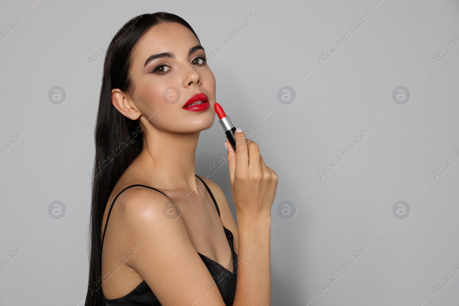 Photo of Young woman with beautiful makeup holding red lipstick on light gray background, space for text