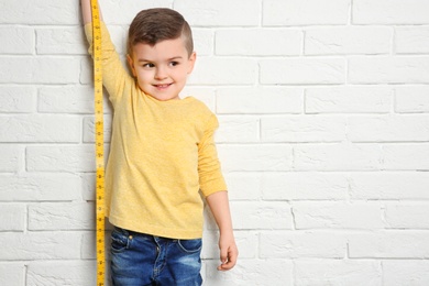 Photo of Little boy measuring his height on brick wall background