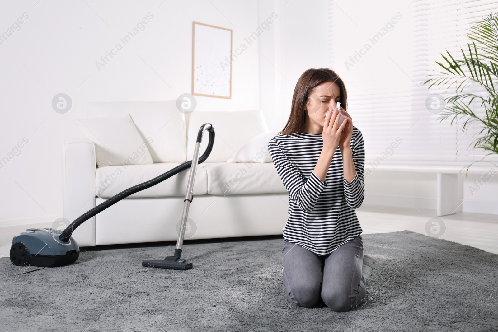 Photo of Young woman suffering from dust allergy while vacuuming house