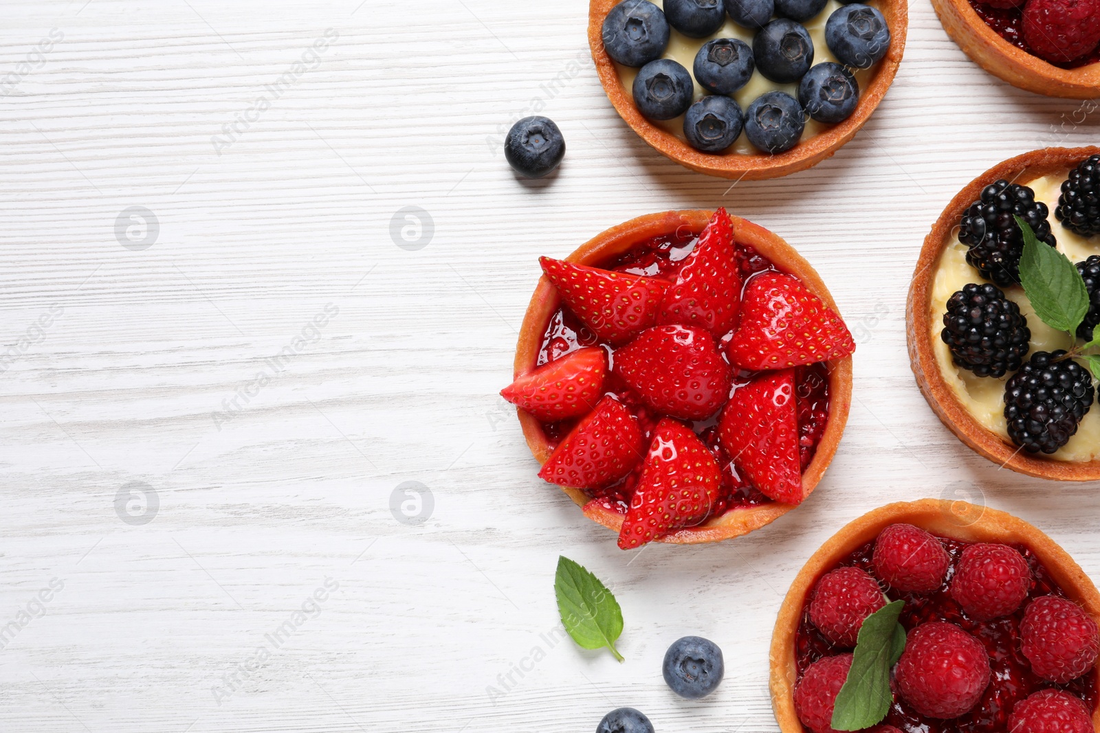 Photo of Tartlets with different fresh berries on white wooden table, flat lay and space for text. Delicious dessert