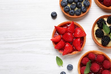 Photo of Tartlets with different fresh berries on white wooden table, flat lay and space for text. Delicious dessert