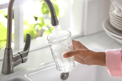 Photo of Woman pouring water into glass in kitchen, closeup