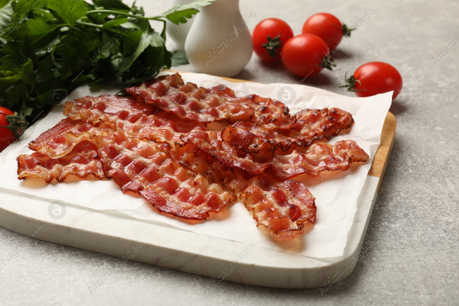 Photo of Fried bacon slices, tomato and parsley on grey textured table, closeup