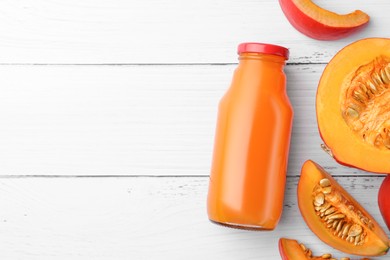 Tasty pumpkin juice in glass bottle and cut pumpkin on white wooden table, flat lay. Space for text