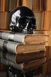 Photo of Black human skull and old books on mirror table