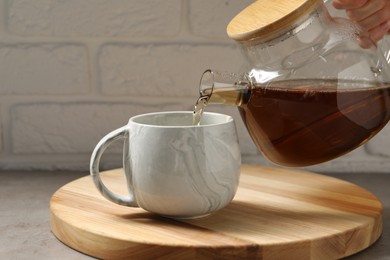 Photo of Woman pouring aromatic tea in cup at table against white brick wall, closeup