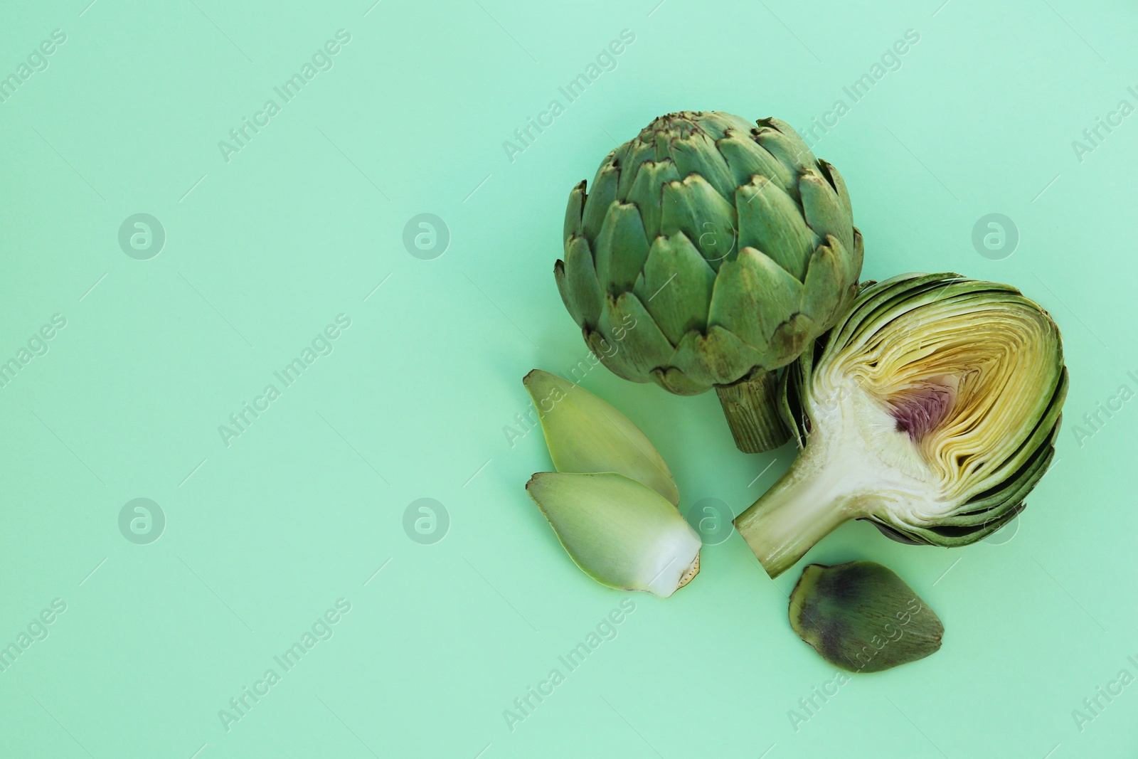 Photo of Whole and cut fresh raw artichokes on pale turquoise background, flat lay. Space for text