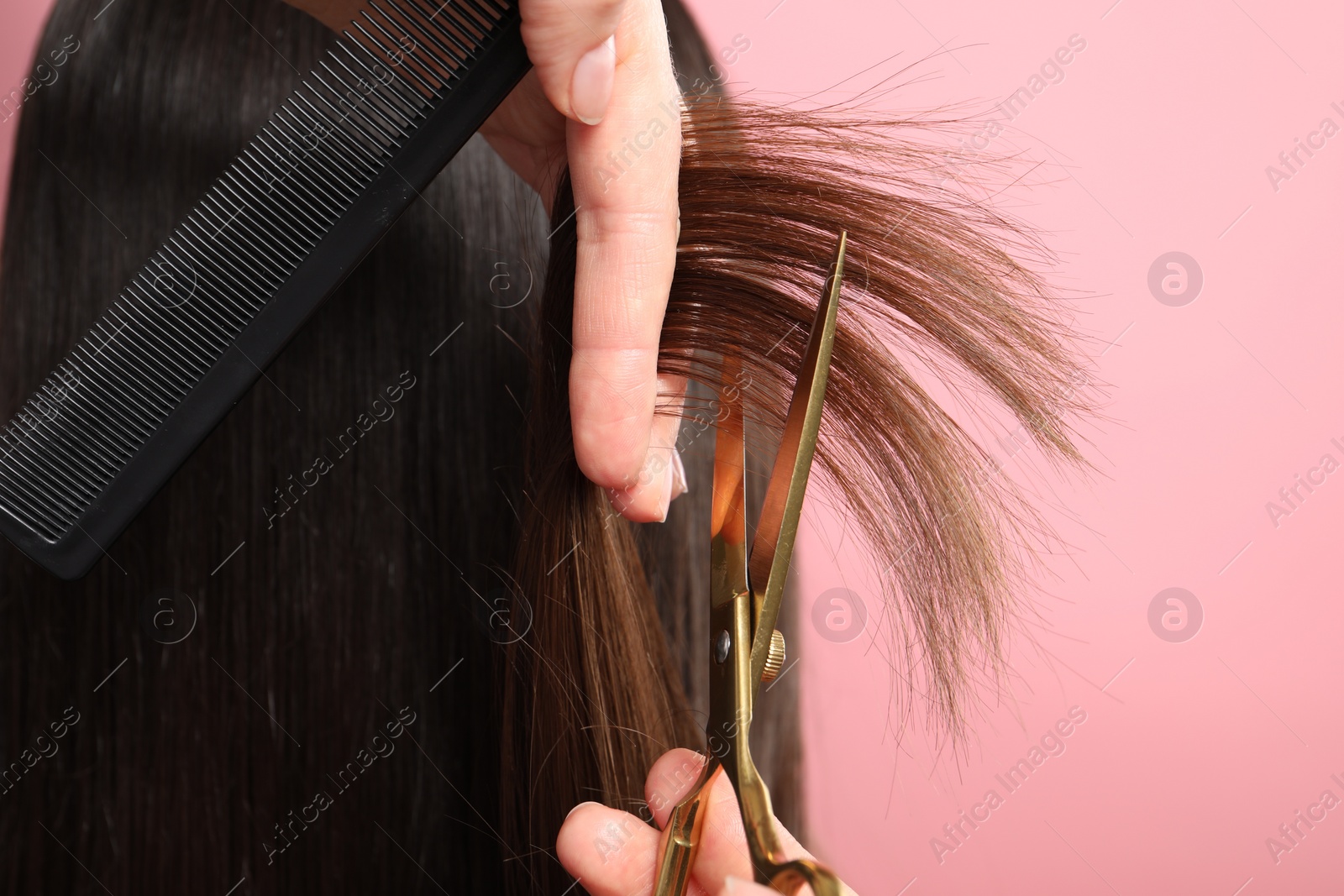 Photo of Hairdresser cutting client's hair with scissors on pink background, closeup