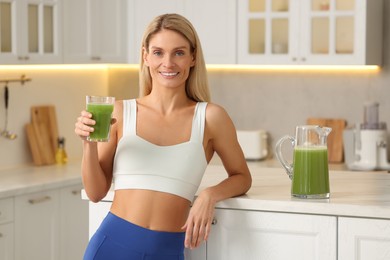 Photo of Happy woman with glass of fresh celery juice in kitchen