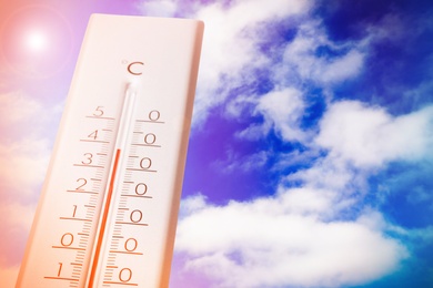 Image of Weather thermometer showing high temperature and blue sky with clouds on background