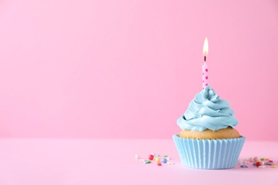 Photo of Delicious birthday cupcake with burning candle and sprinkles on pink background, space for text