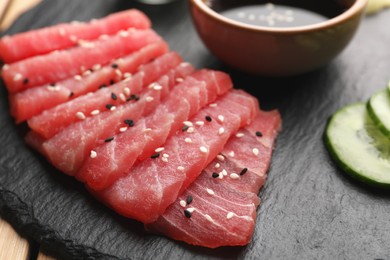 Photo of Tasty sashimi (pieces of fresh raw tuna with sesame seeds) on black board, closeup