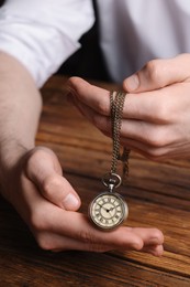 Man holding chain with elegant pocket watch at wooden table, closeup