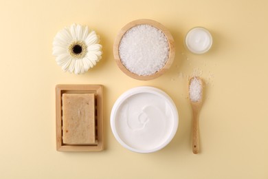 Jars of cream, body care products and gerbera flower on beige background, flat lay