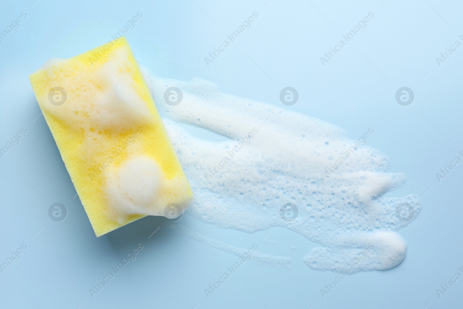 Photo of Yellow sponge with foam on light blue background, top view