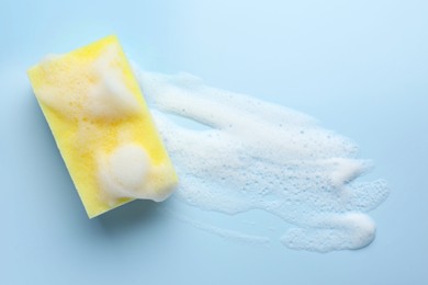 Yellow sponge with foam on light blue background, top view