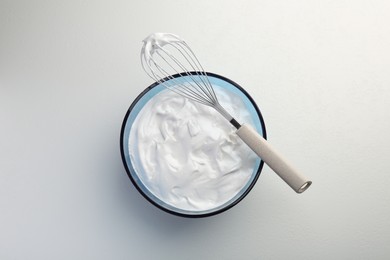 Bowl with whipped cream and whisk on light background, top view