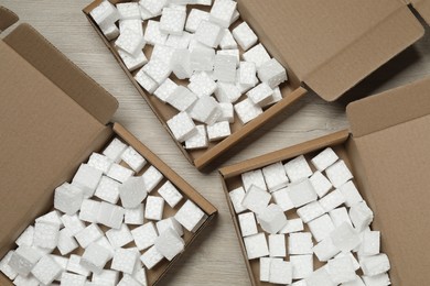 Photo of Open cardboard boxes with pieces of polystyrene foam on wooden floor, flat lay. Packaging goods