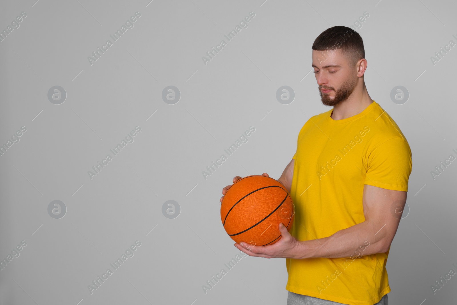 Photo of Athletic young man with basketball ball on light grey background. Space for text