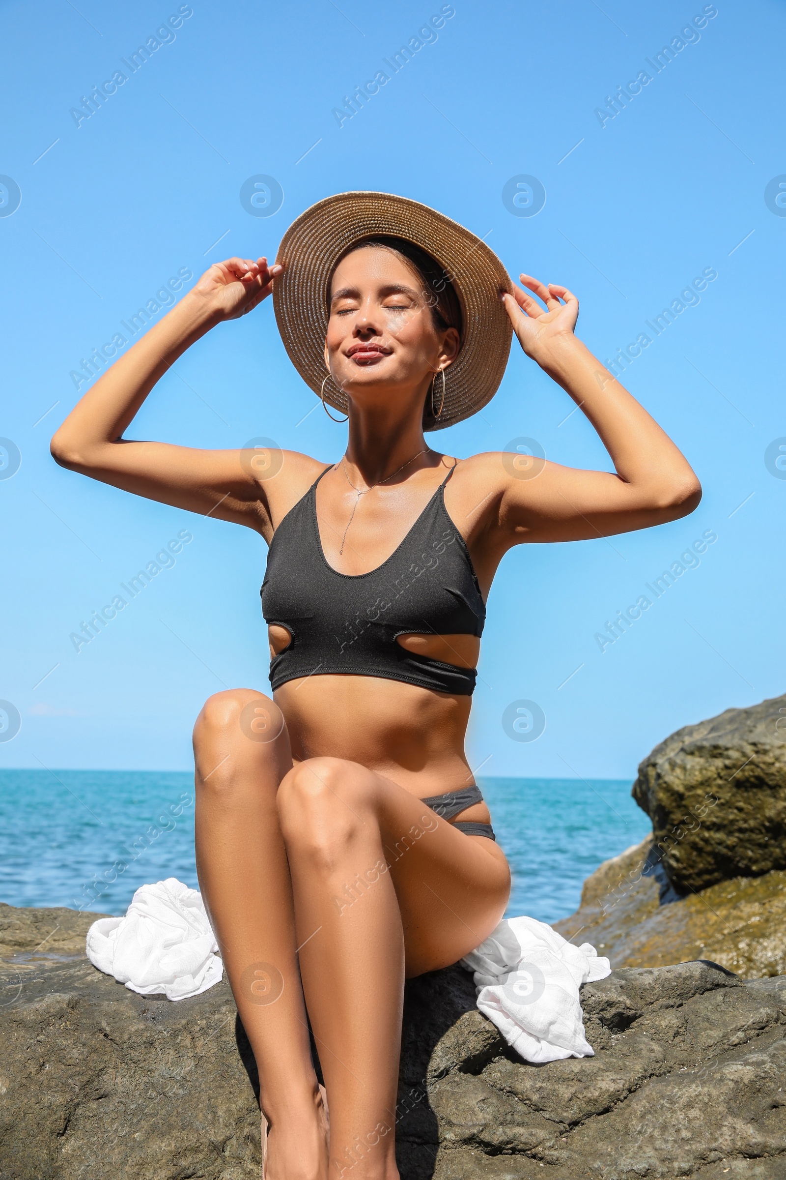 Photo of Beautiful young woman in stylish bikini sitting on rock near sea