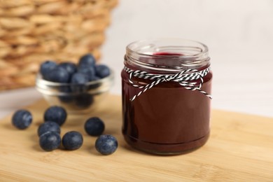 Photo of Jar with tasty blueberry jam and berries on wooden table. Space for text