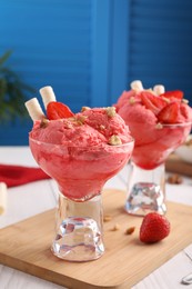 Photo of Delicious scoops of strawberry ice cream with wafer sticks and nuts in glass dessert bowls served on white table