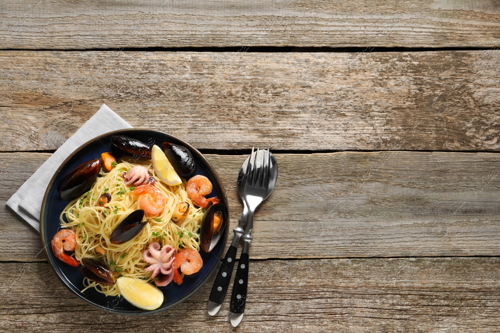 Photo of Delicious spaghetti with seafood served on wooden table, flat lay. Space for text