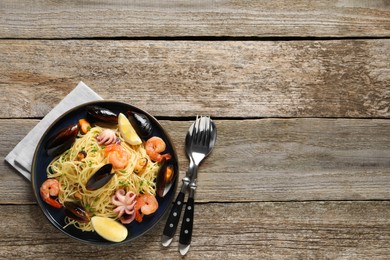 Delicious spaghetti with seafood served on wooden table, flat lay. Space for text