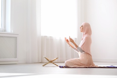 Muslim woman in hijab praying on mat indoors