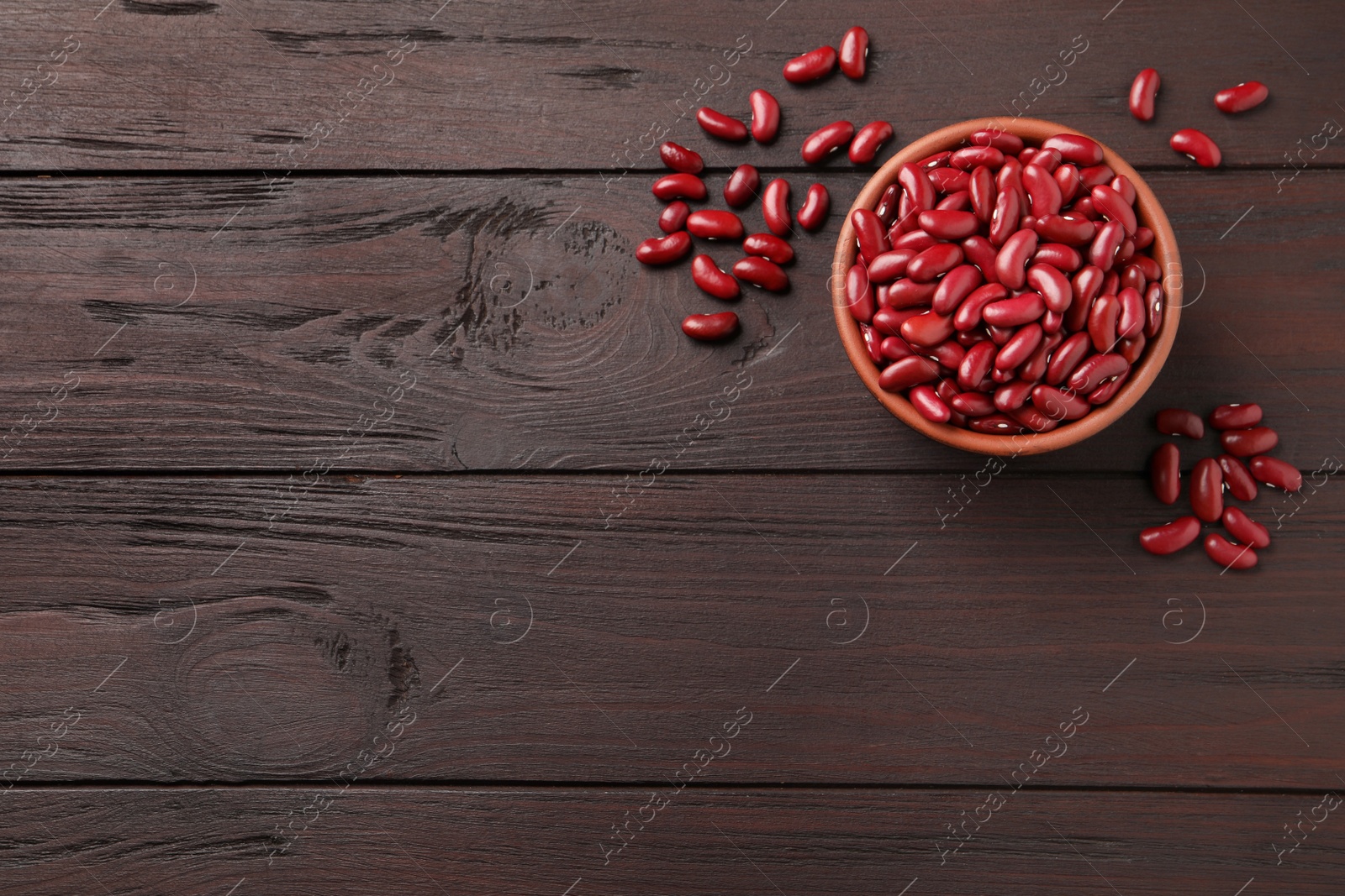 Photo of Raw red kidney beans with bowl on wooden table, flat lay. Space for text