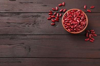 Photo of Raw red kidney beans with bowl on wooden table, flat lay. Space for text