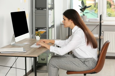 Young woman with bad posture sitting at workplace in office. Symptom of scoliosis