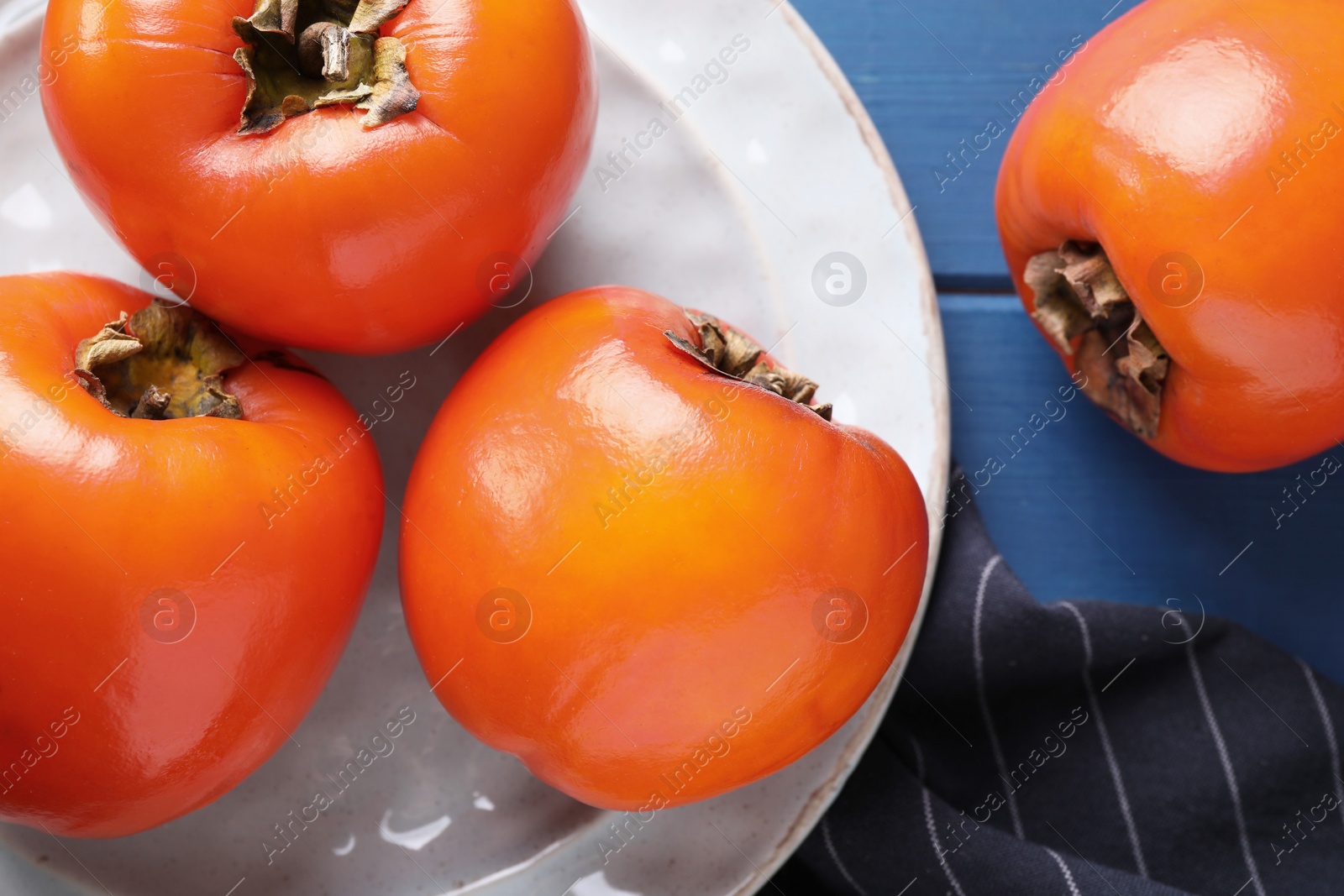 Photo of Delicious ripe persimmons on blue wooden table, top view