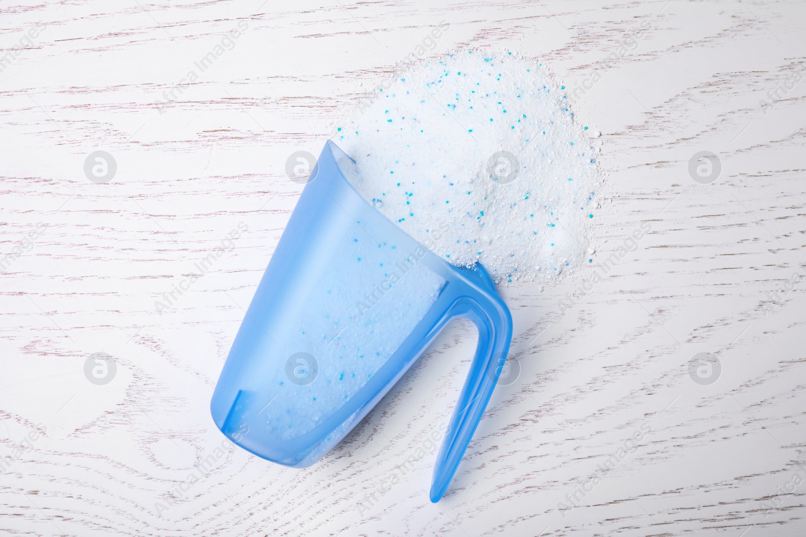 Photo of Measuring cup with laundry powder on white wooden background, top view