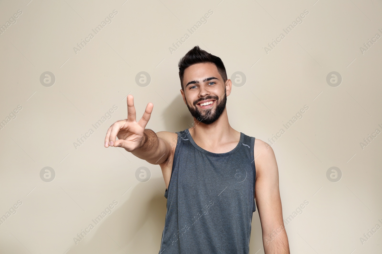 Photo of Happy young man showing victory gesture on color background