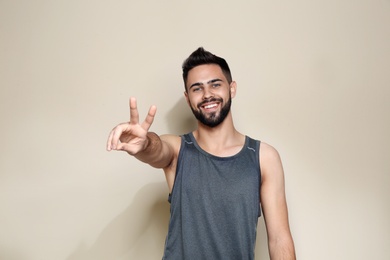 Photo of Happy young man showing victory gesture on color background