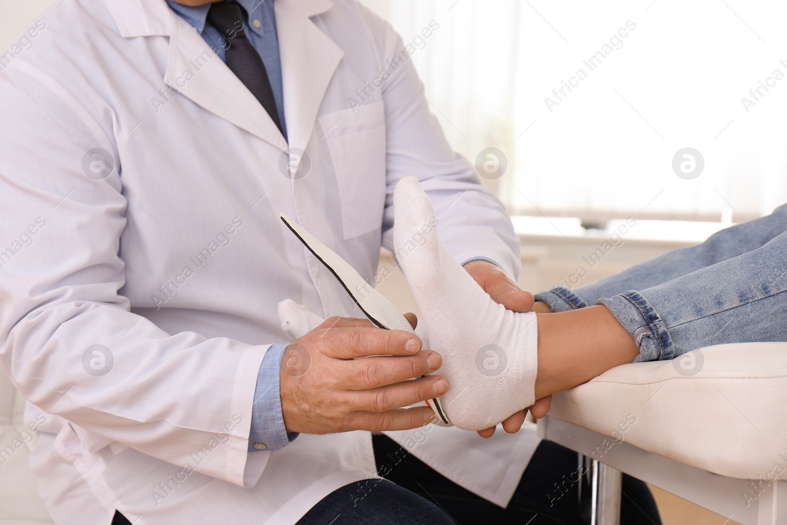 Photo of Male orthopedist fitting insole on patient's foot in clinic, closeup