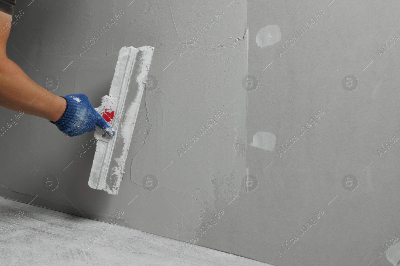 Photo of Professional worker plastering wall with putty knife, closeup