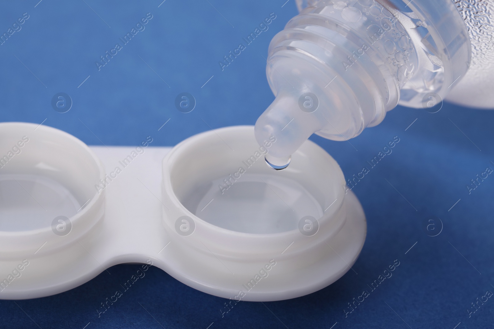Photo of Dripping solution into case with contact lenses on blue background, closeup