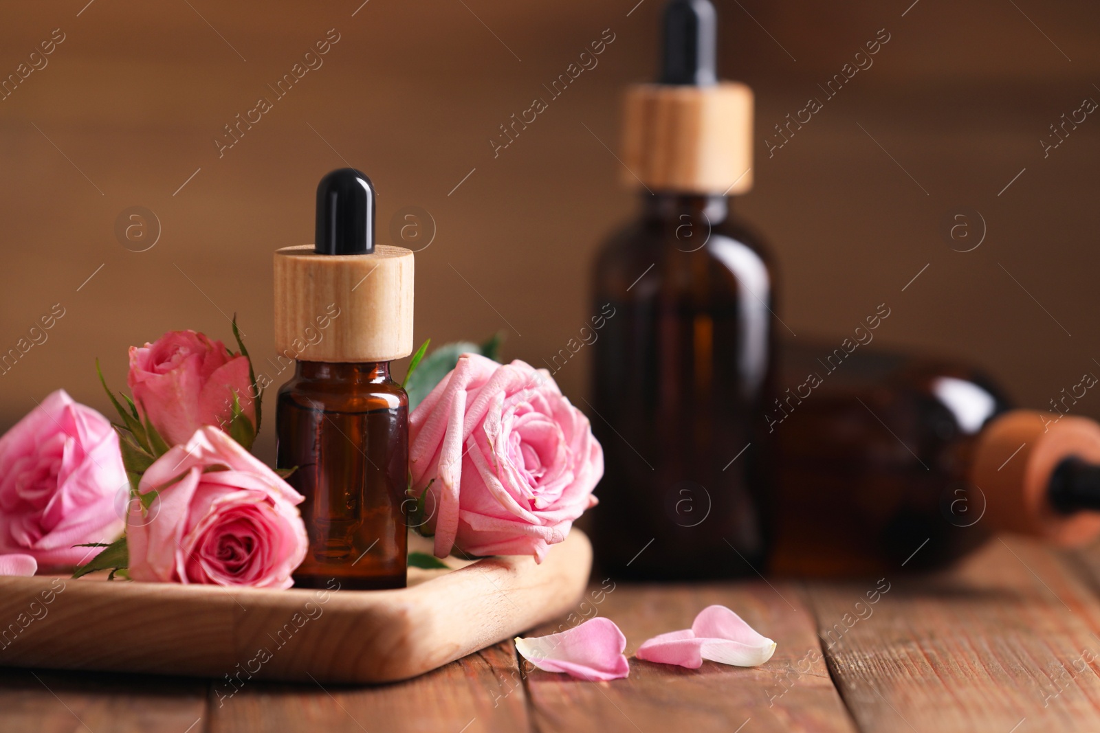 Photo of Bottles of essential rose oil and flowers on wooden table